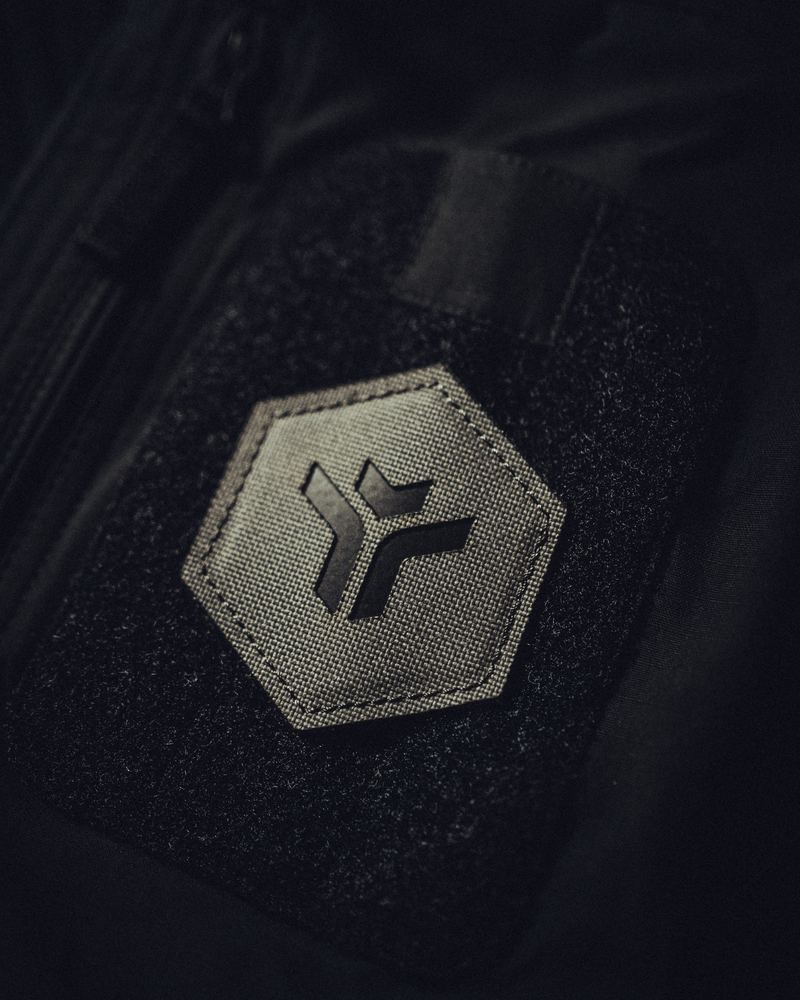 Sechseckiger Patch mit der Tacticool-Bildmarke, auf einem Klettfeld an einer dunklen Jacke